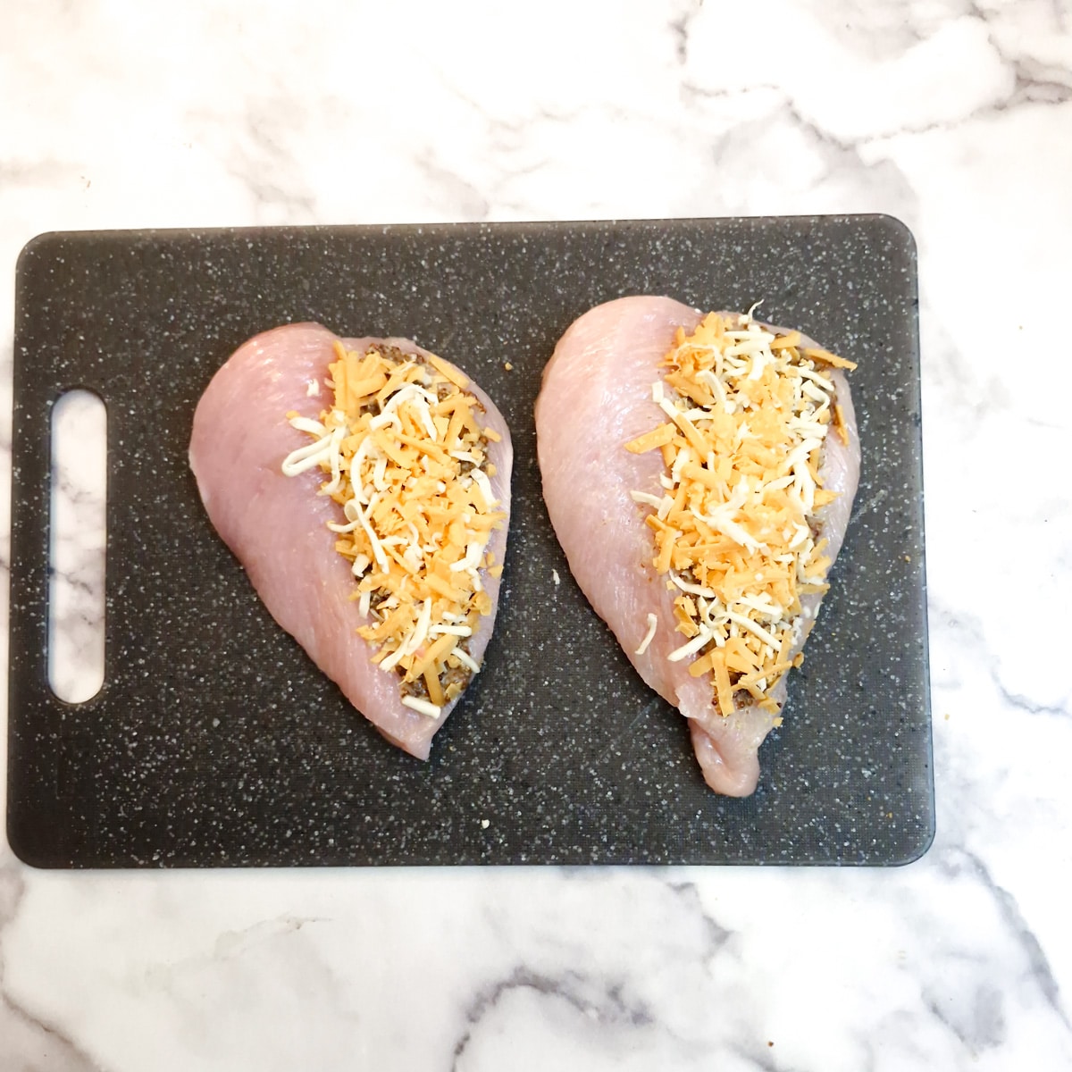 Two butterflied chicken breasts each with grated cheese on top of the mustard.