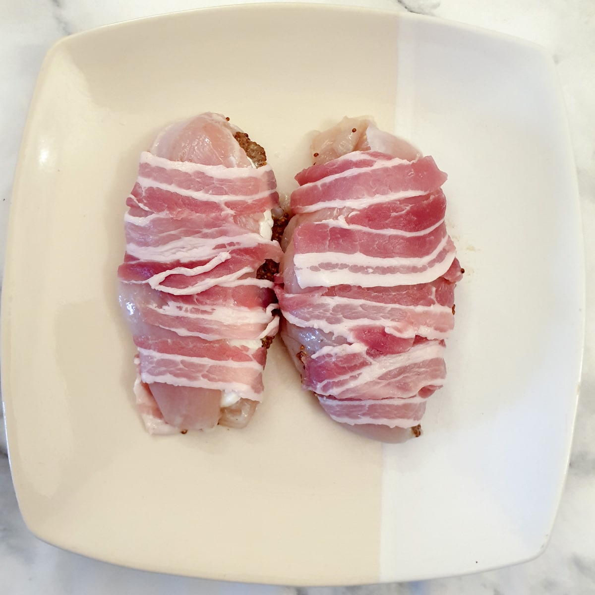 Two bacon wrapped chicken breasts on a plate.