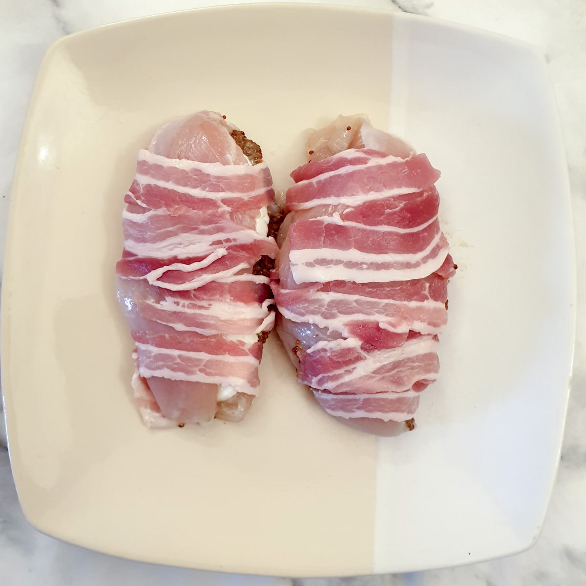 Two bacon wrapped chicken breasts on a plate.