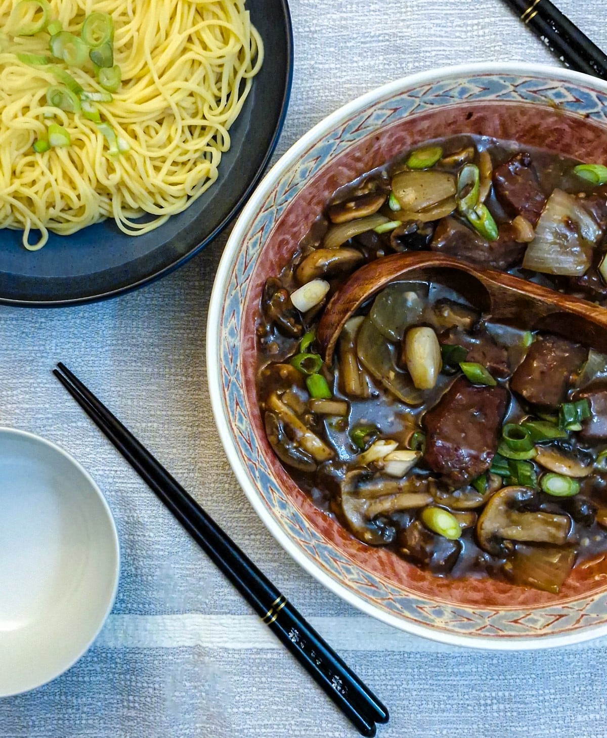 A serving dish of beef and mushroom stirfry alongside a dish of noodles.