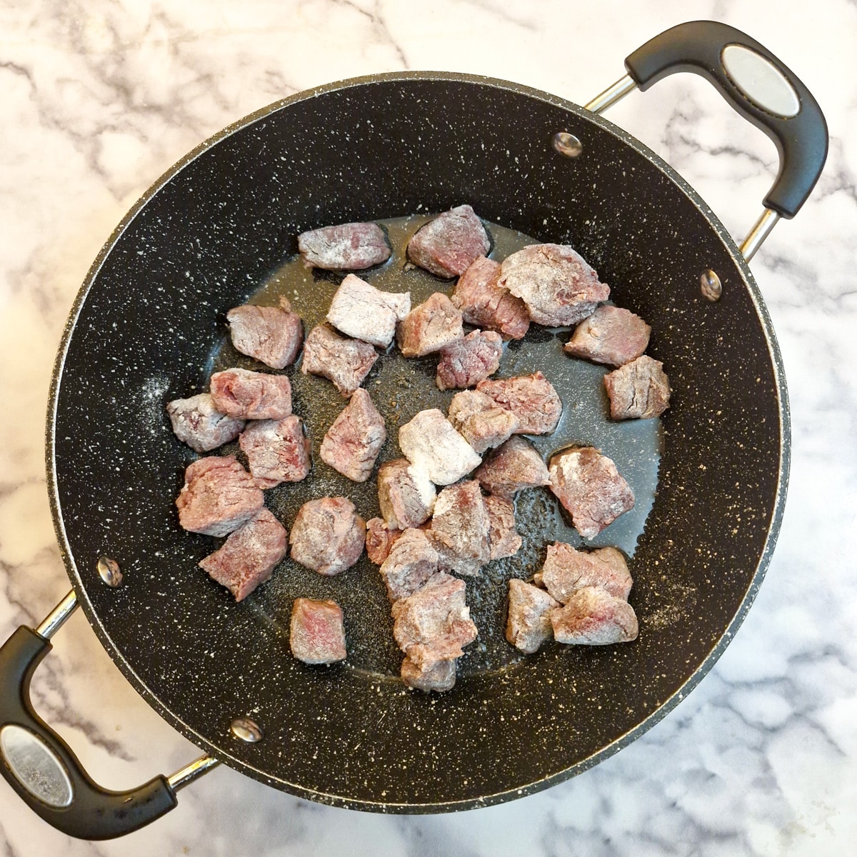 Pieces of meat which have been coated in seasoned flour in a frying pan.