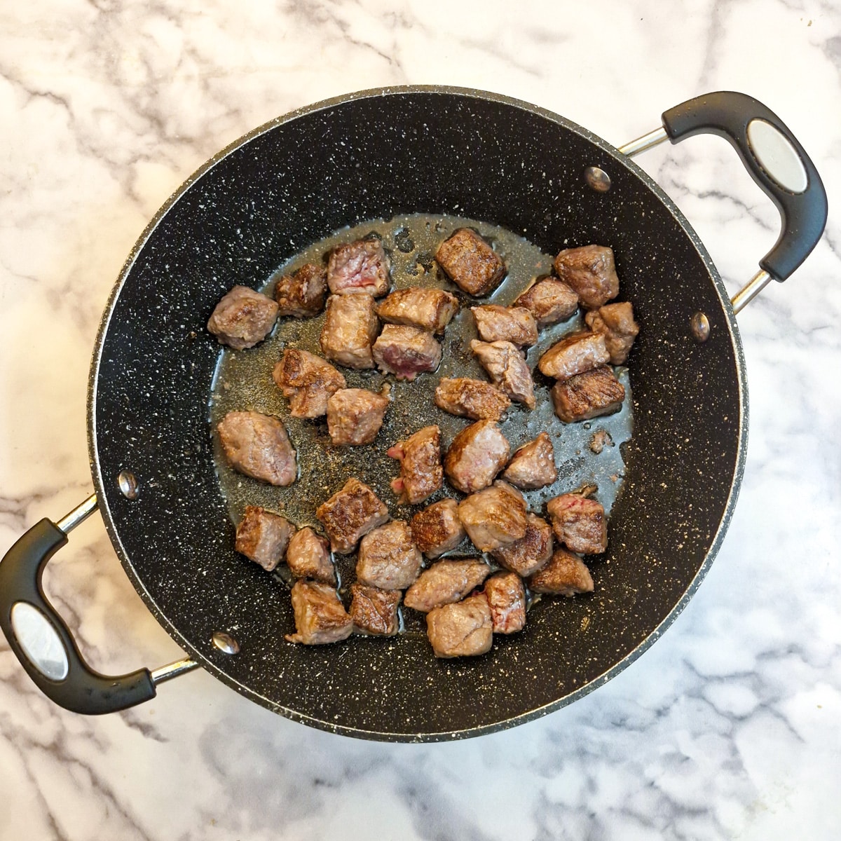 Pieces of browned beef in a frying pan.