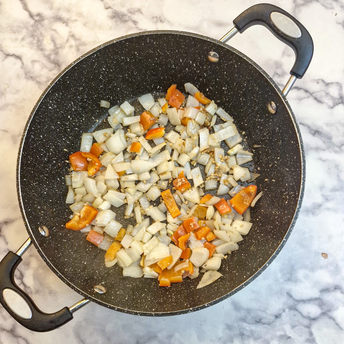 Chopped red pepper and onions softening in a frying pan.