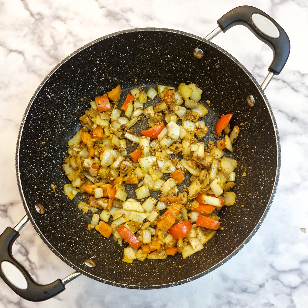 Spices added tp the pepper and onions in a frying pan.