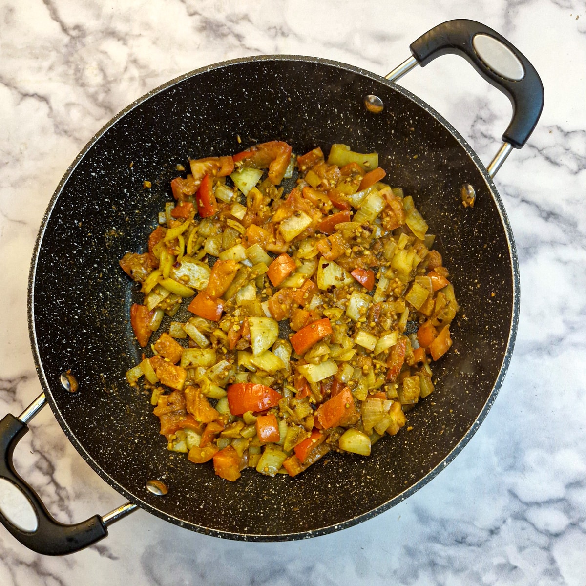 Tomatoes softening with spiced onions and peppers in a frying pan.