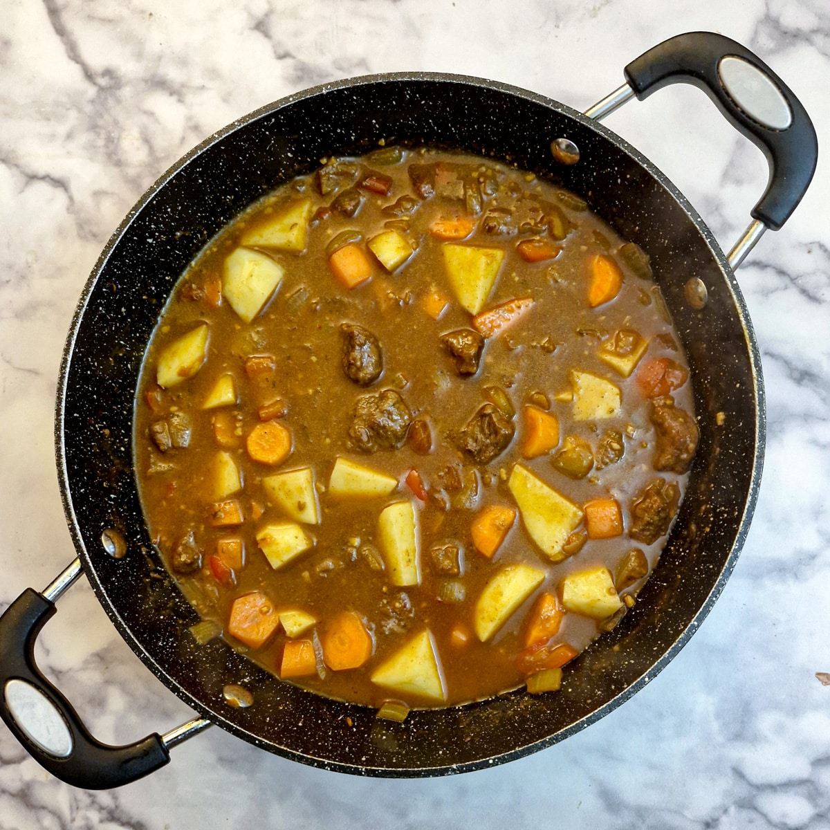 Diced potatoes and carrots added to the beef curry in a frying pan.