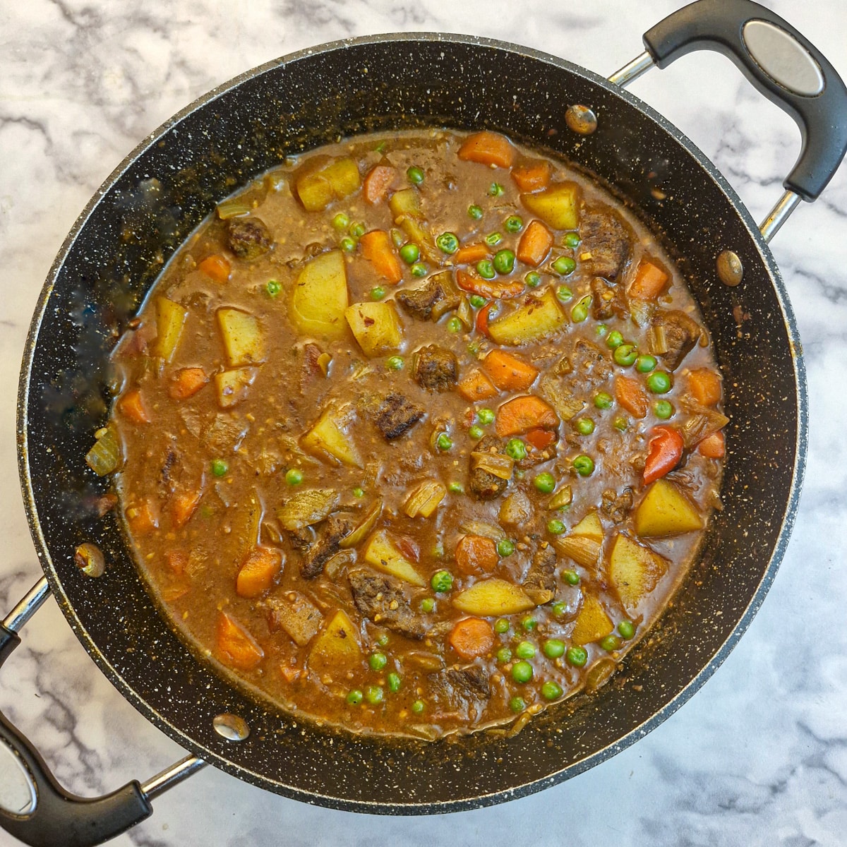 The completed beef curry in a frying pan with the addition of peas.