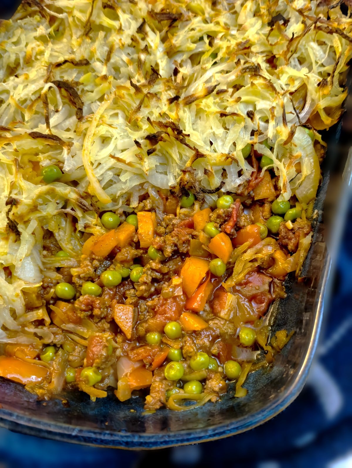 A glass baking dish containing beef keema with a crispy rosti topping. The corner of the rosti has been removed to show the beef keema on the inside.