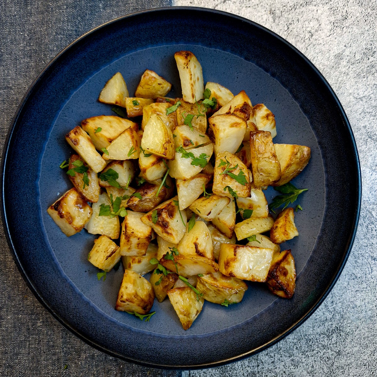 Overhead shot of a blue serving dish filled with butter roast potatoes on a grey background.