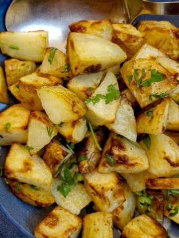 A blue serving dish filled with butter roast potatoes.