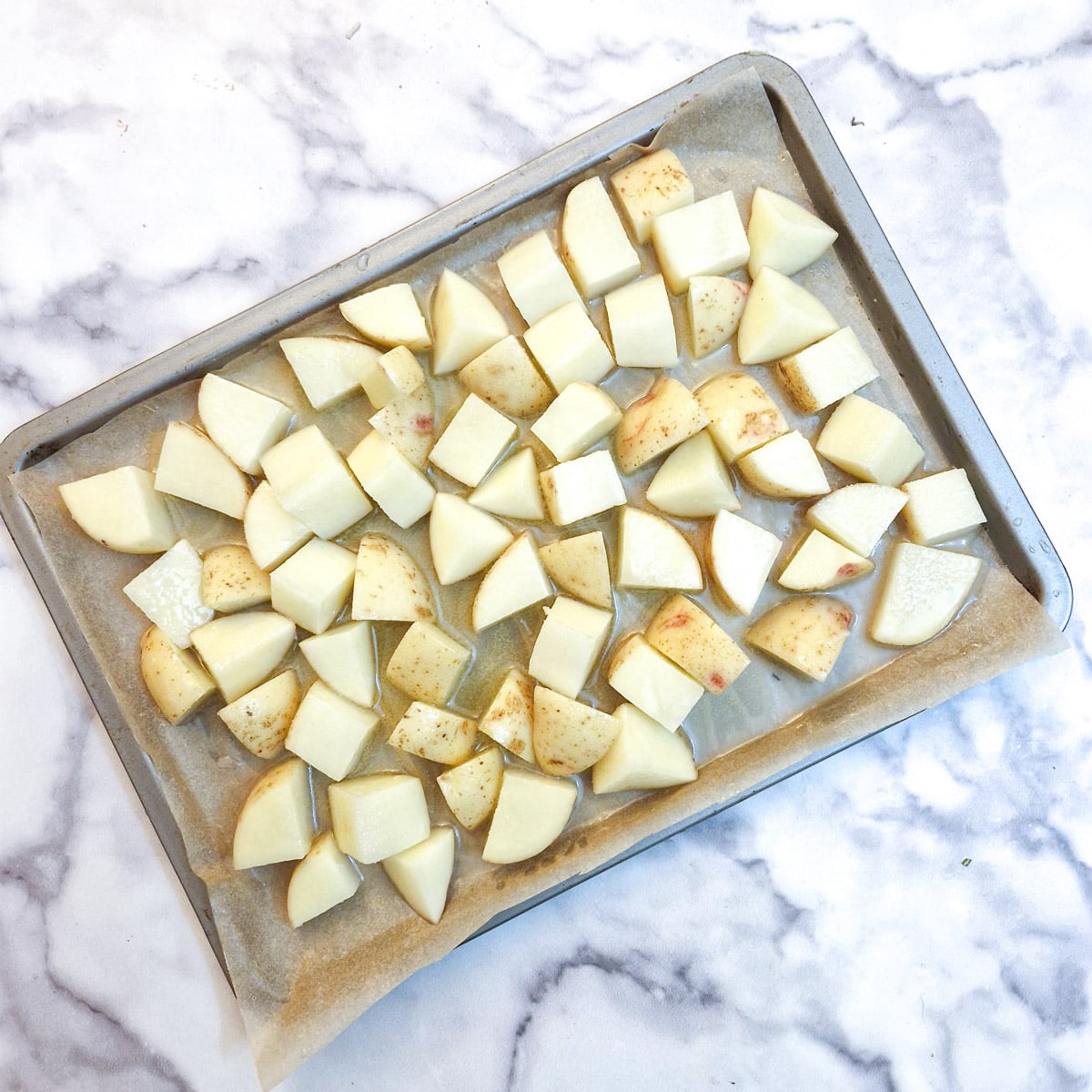 A single layer of cubed potatoes on a baking tray.