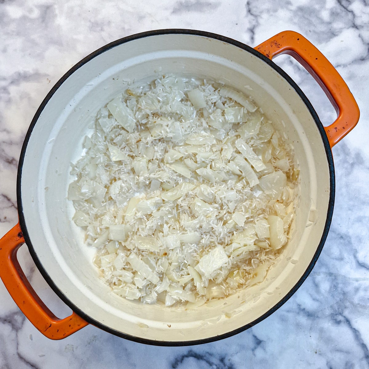 Rice mixed with onions in a casserole dish.