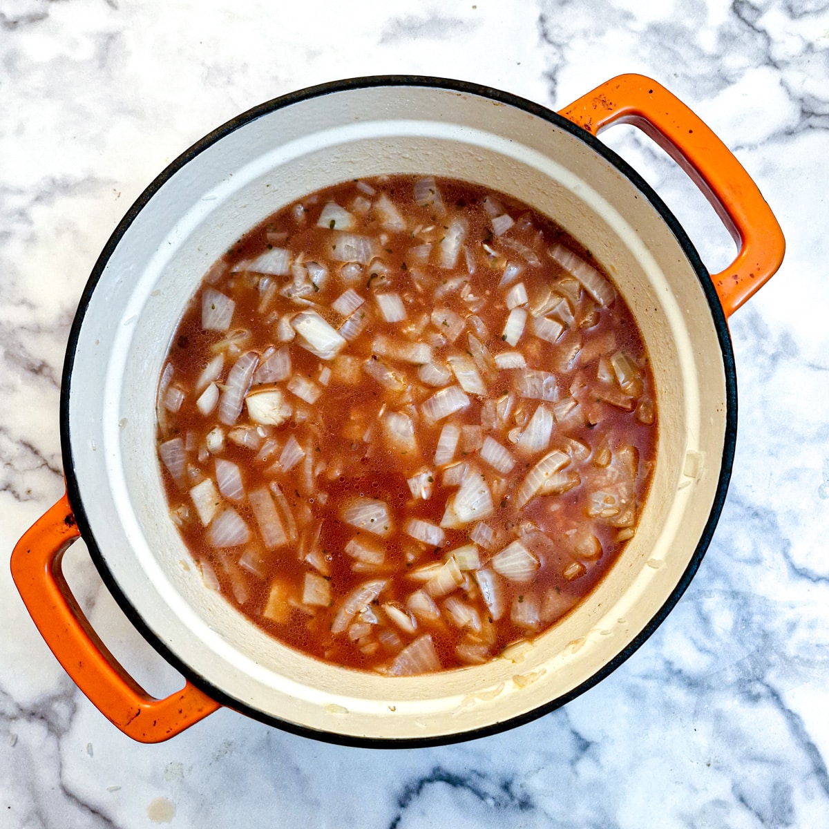 Stock added to onions and rice in a casserole dish.