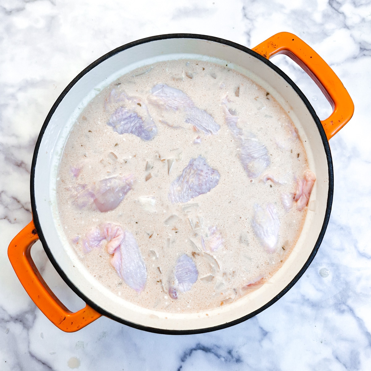 Raw chicken pieces nestled into the sauce in a casserole dish.