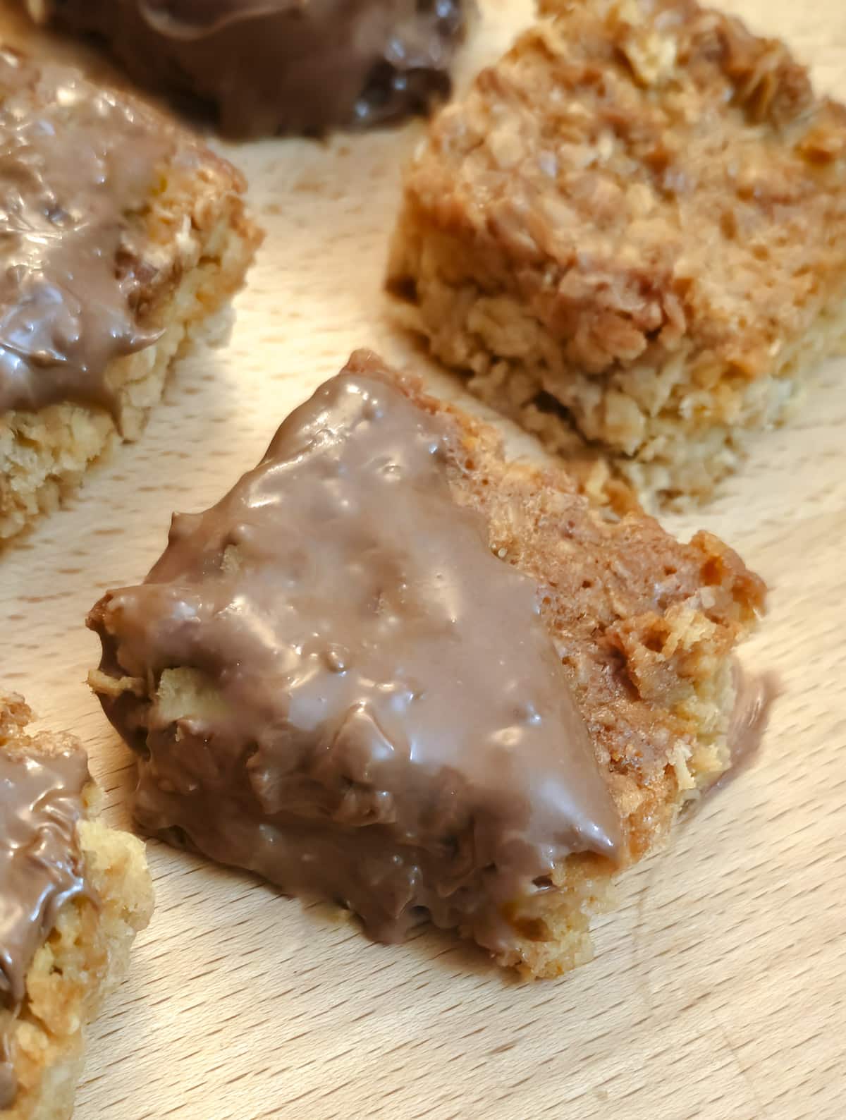 Close up of a chocolate-coated condensed milk flapjack on a wooden board.