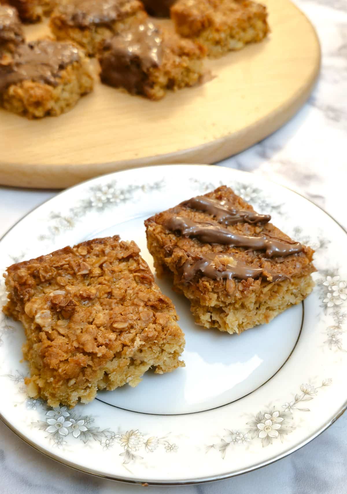 Two flapjacks on a patterned plate in from of a wooden board holding more flapjacks.