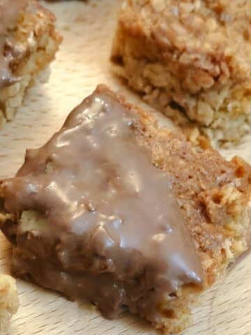 Close up of a chocolate-coated condensed milk flapjack on a wooden board.