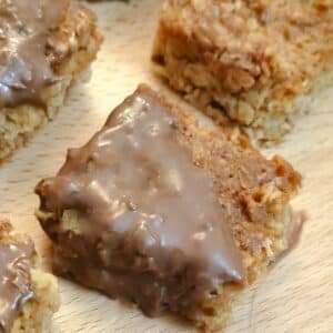 Close up of a chocolate-coated condensed milk flapjack on a wooden board.