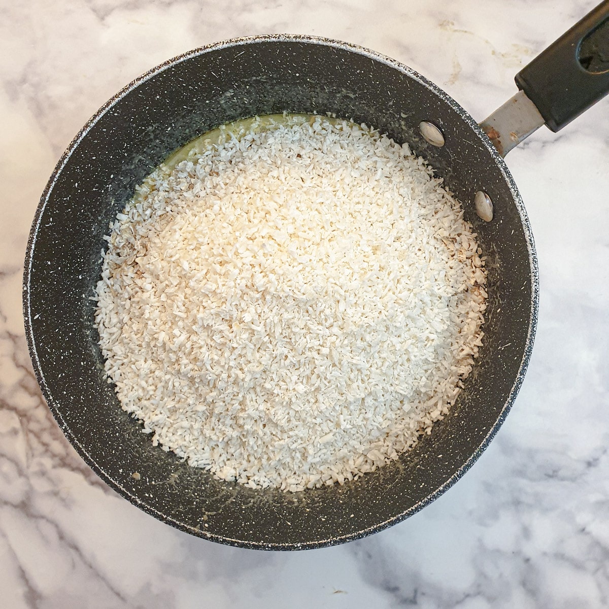 Coconut and oats added to the butter mixture in a saucepan.