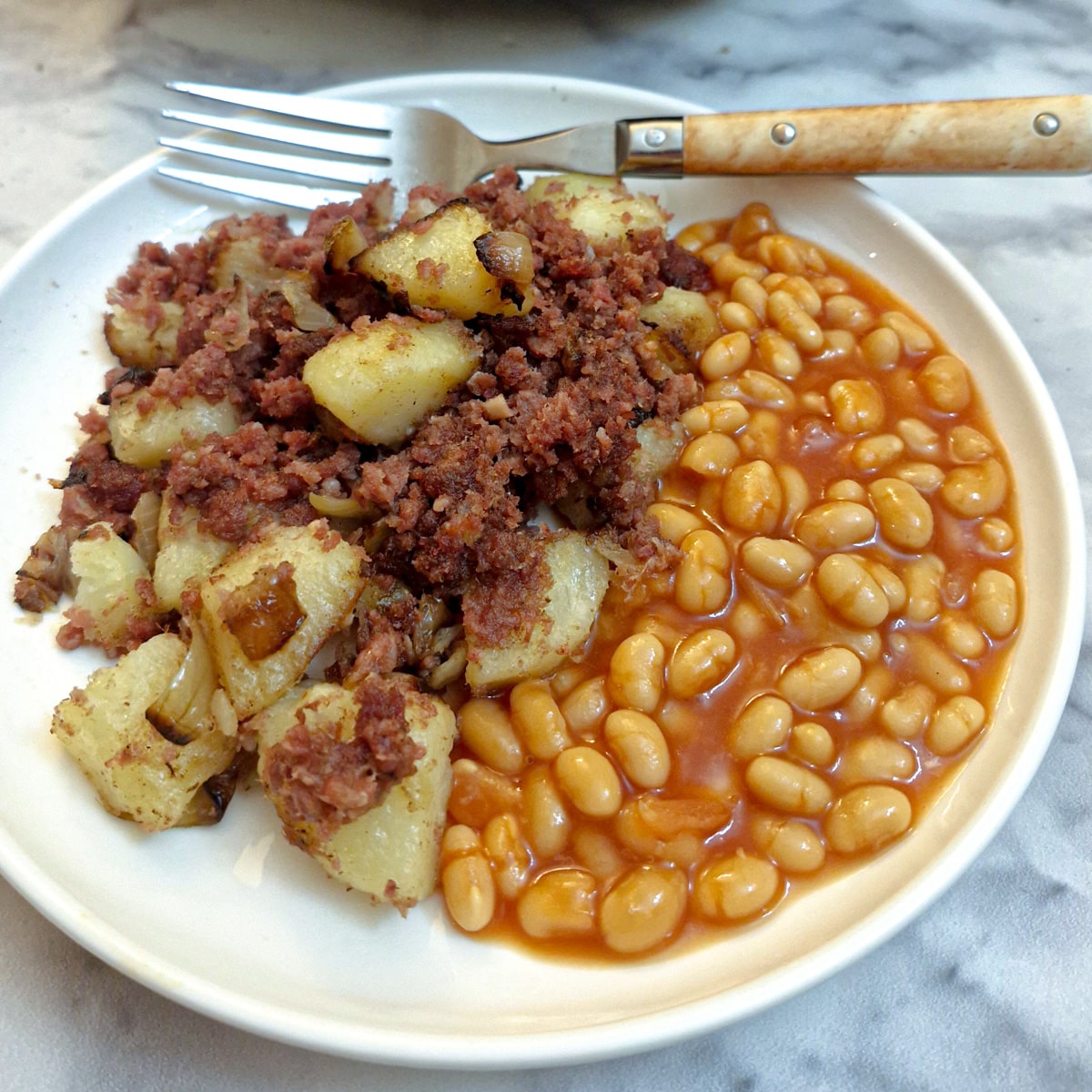 A white plate with a helping of corned beef hash and a side of baked beans.