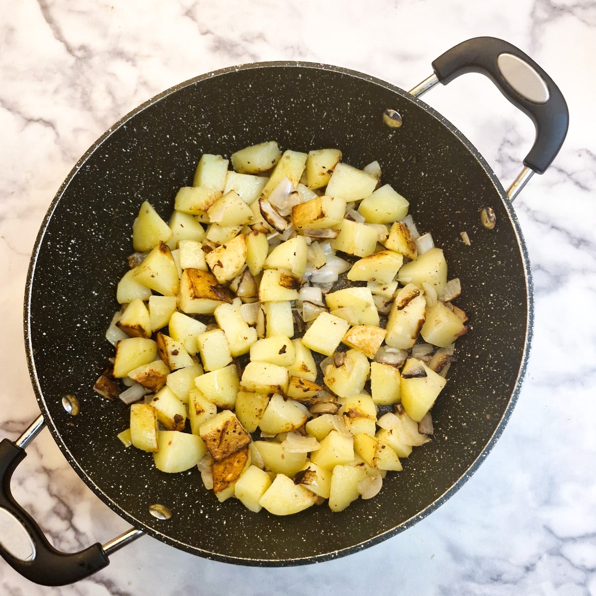 Browned potatoes and onions in a frying pan.