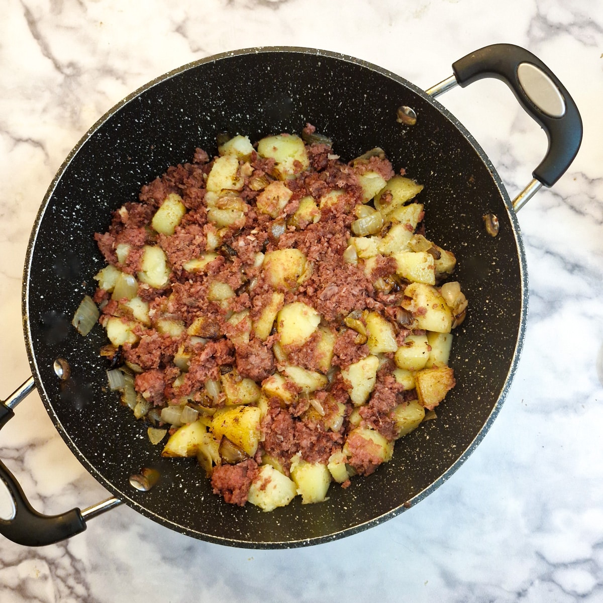 Corned beef mixed with potatoes and onions in a frying pan.