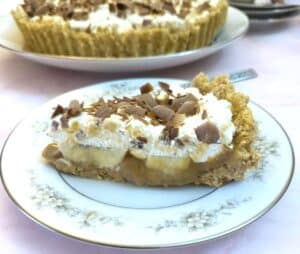 A closeup of a slice of banoffee pie on a plate with the full pie in the background.