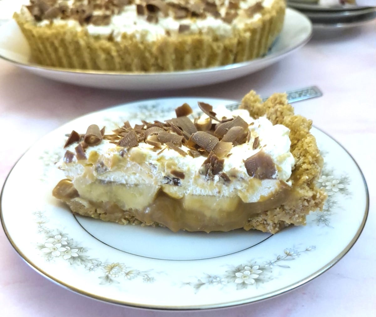 A closeup of a slice of banoffee pie on a plate with the full pie in the background.