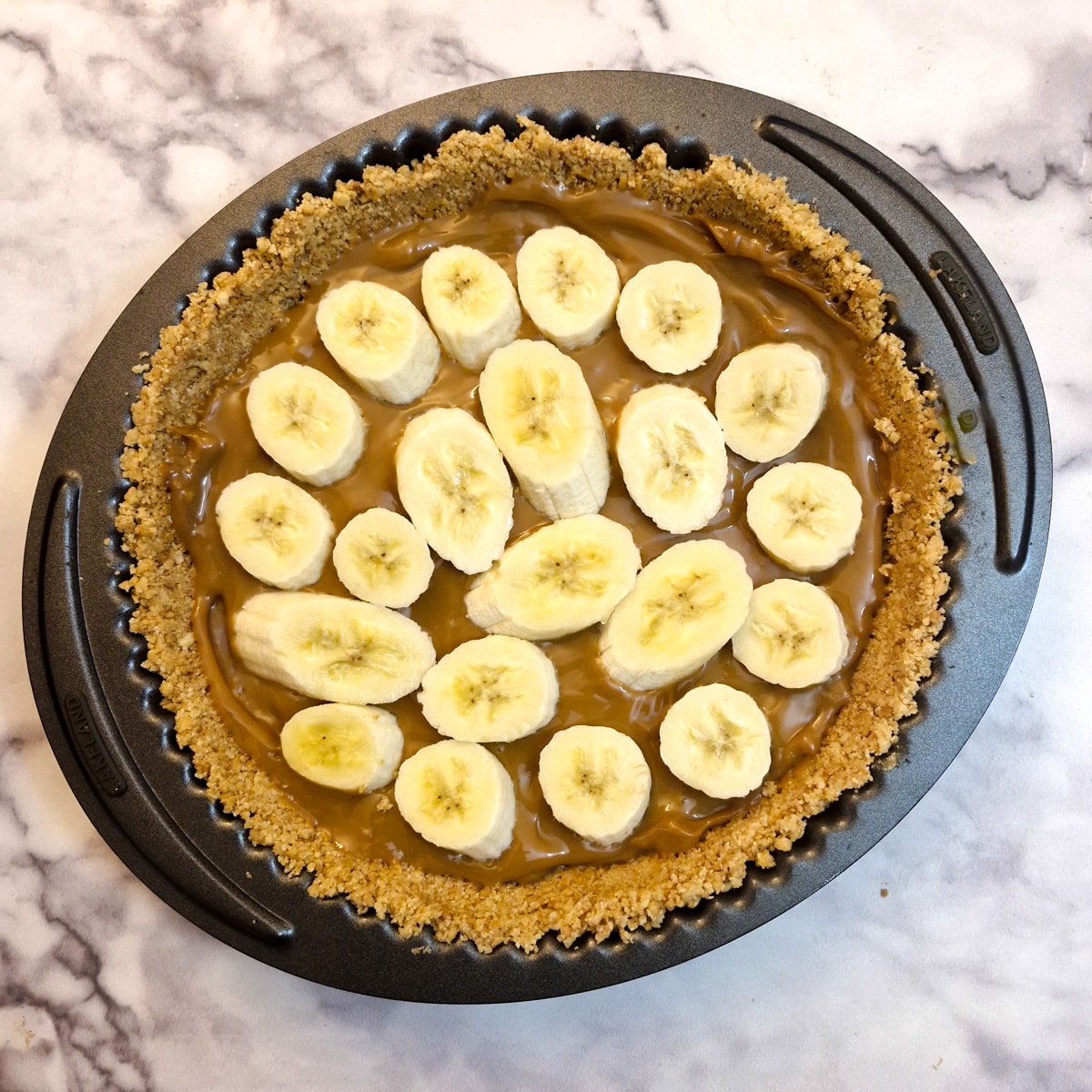 Sliced bananas arranged on caramel in a flan dish.