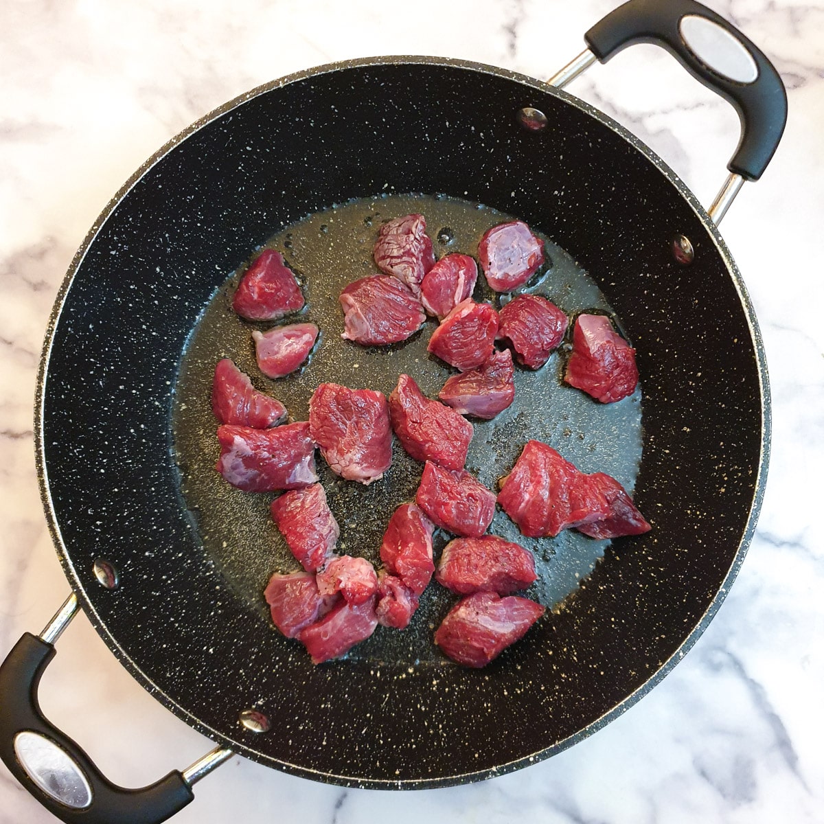 Cubes of raw steak in a frying pan.