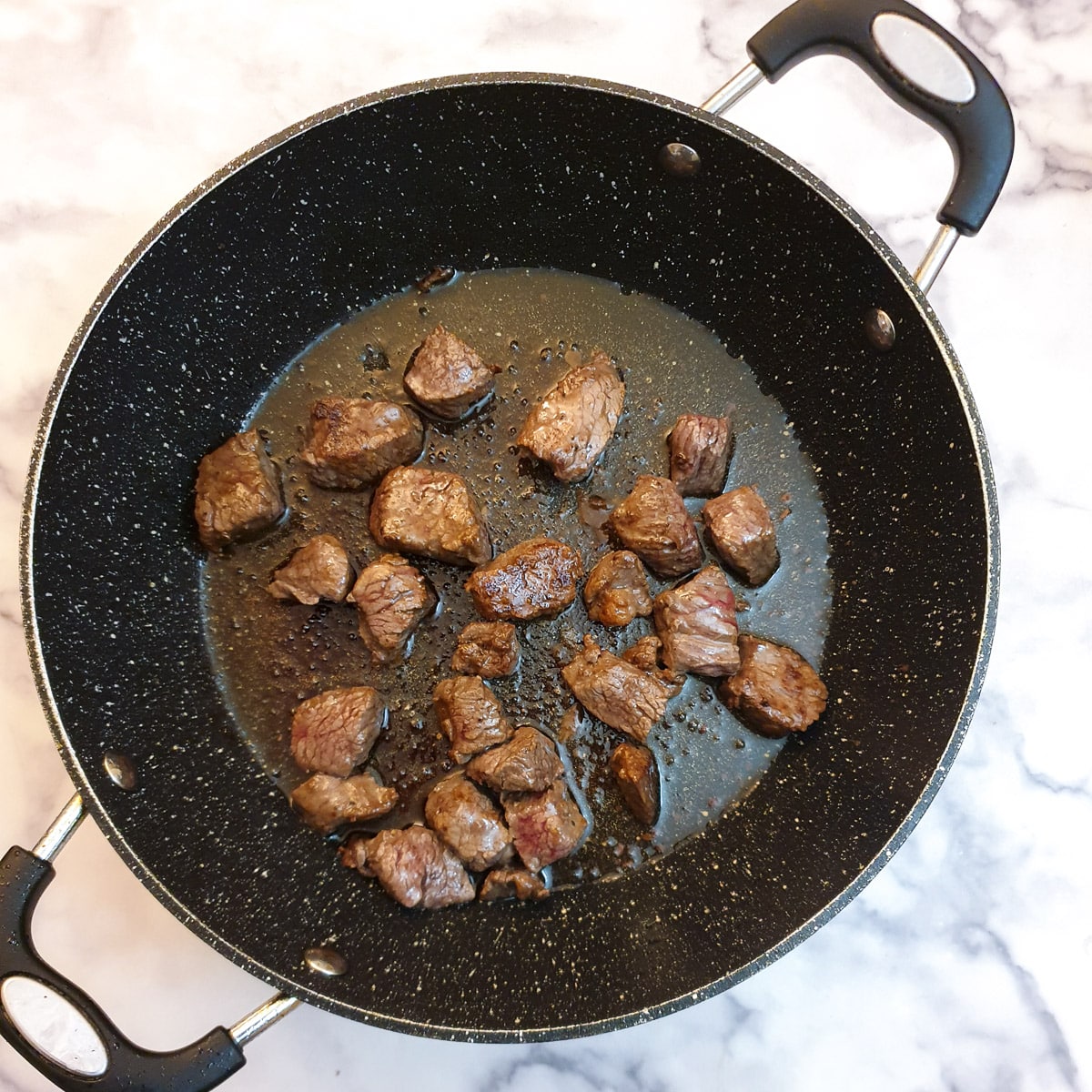 Cubes of brown seared steak in a frying pan.