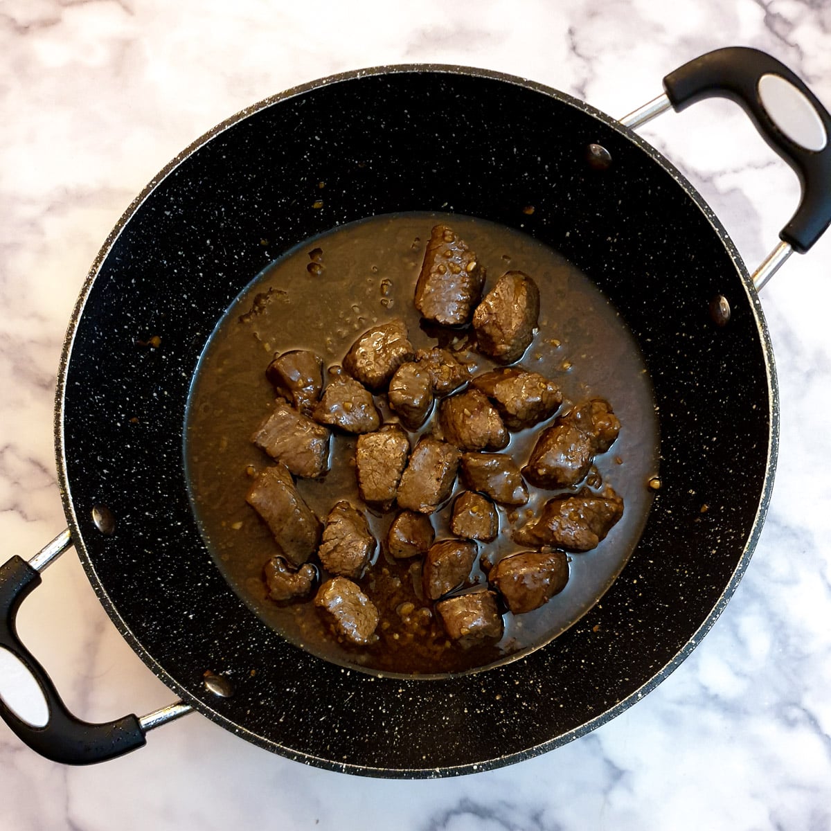 Cubes of steak mixed with sauce in a frying pan.