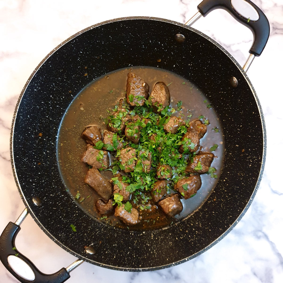 Chopped parsley added to steak in a frying pan.