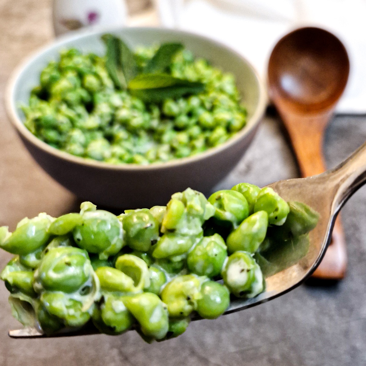 Close up of minted smashed peas on a fork with a dish of peas in the background.