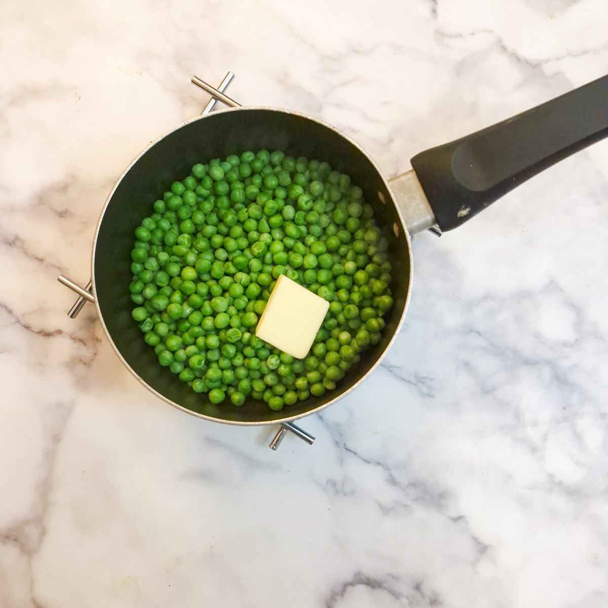 A small saucepan containing frozen peas and a knob of butter.