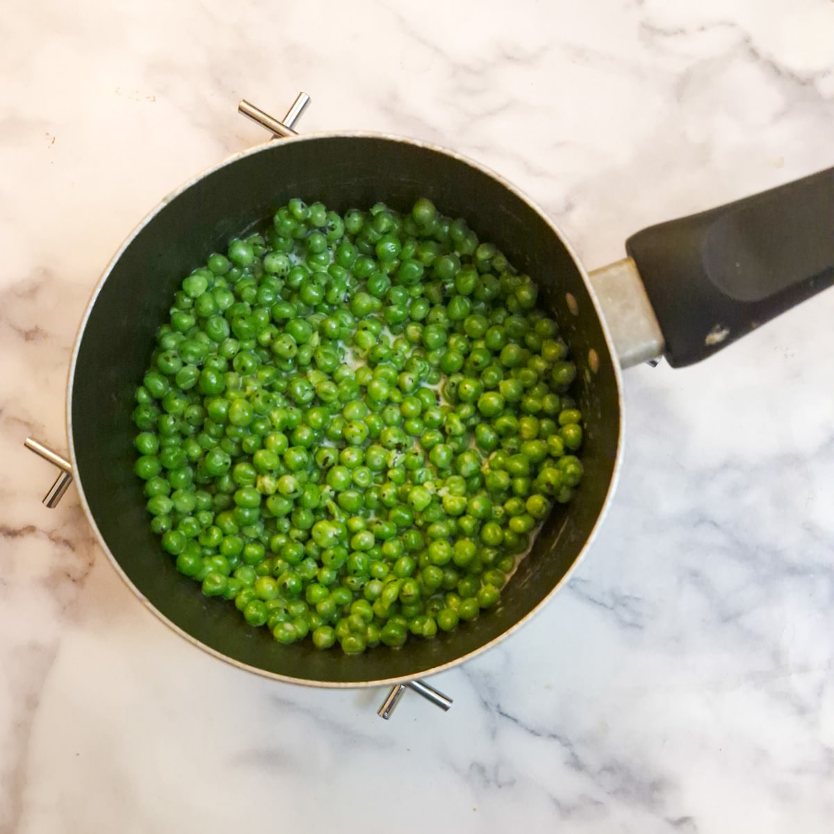 Cream and mint sauce added to peas in a saucepan.