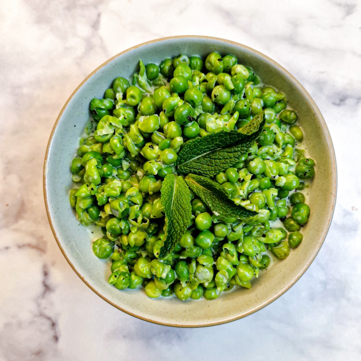 Overhead shot of a small bowl of minted smashed peas garnished with fresh mint leaves.