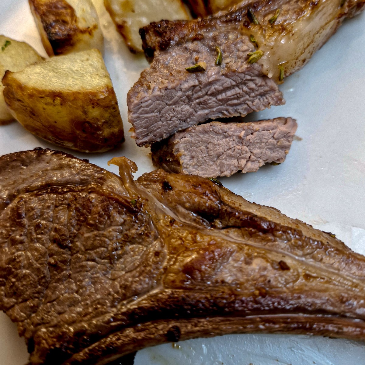 Close up of a lamb chop that has been cut in half to show the texture.  There is a complete lamb chop in the foreground.