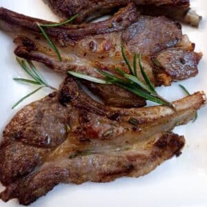 Close up of two pan-fried lamb chops on a white plate with sprigs of rosemary.