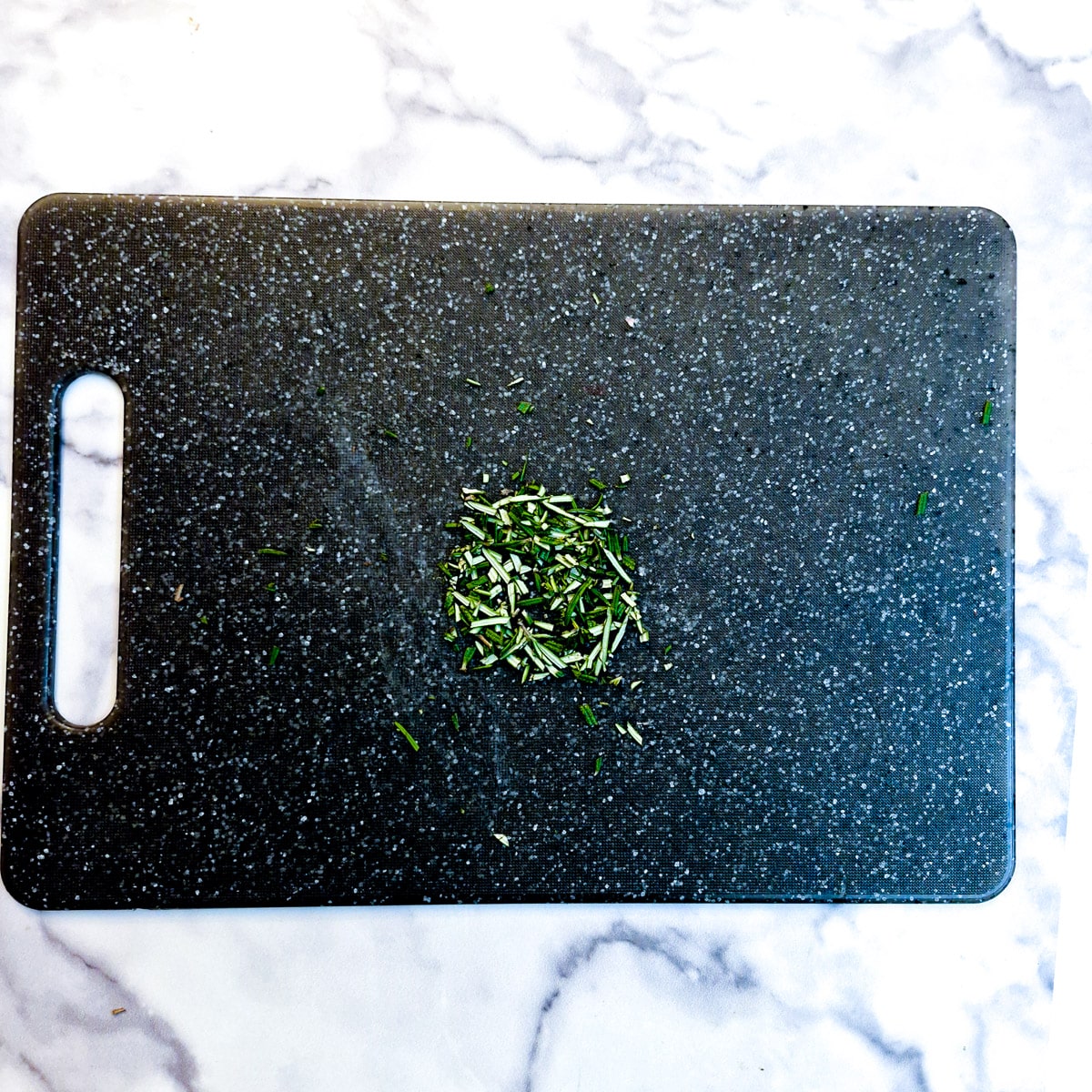 A small pile of chopped rosemary on a chopping board.