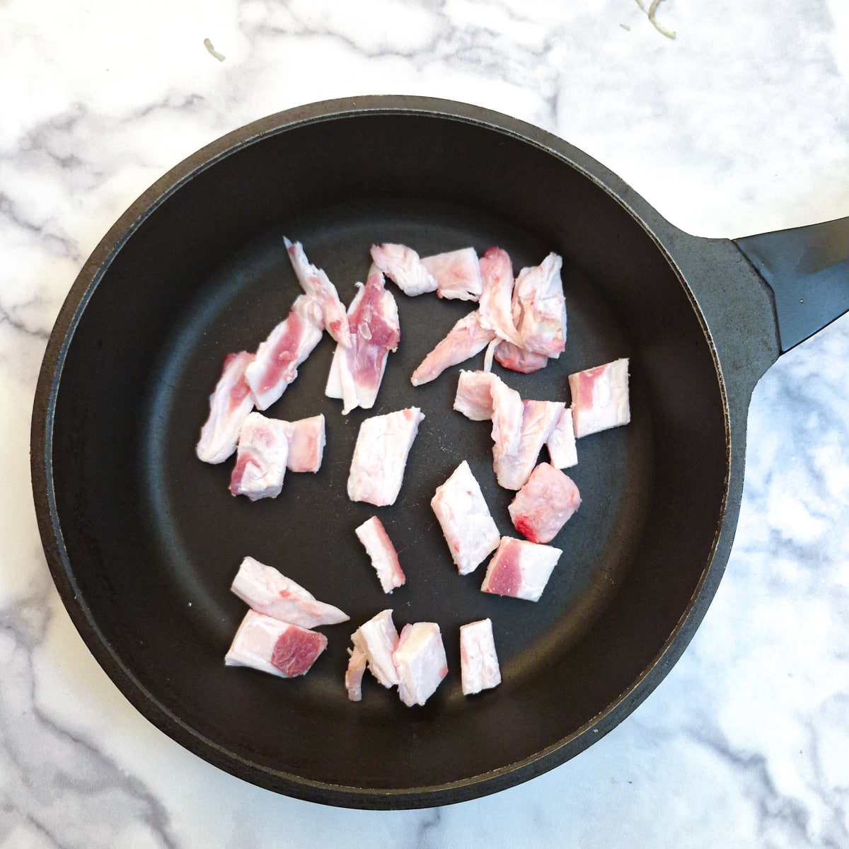 Pieces of uncooked lamb fat in a frying pan.