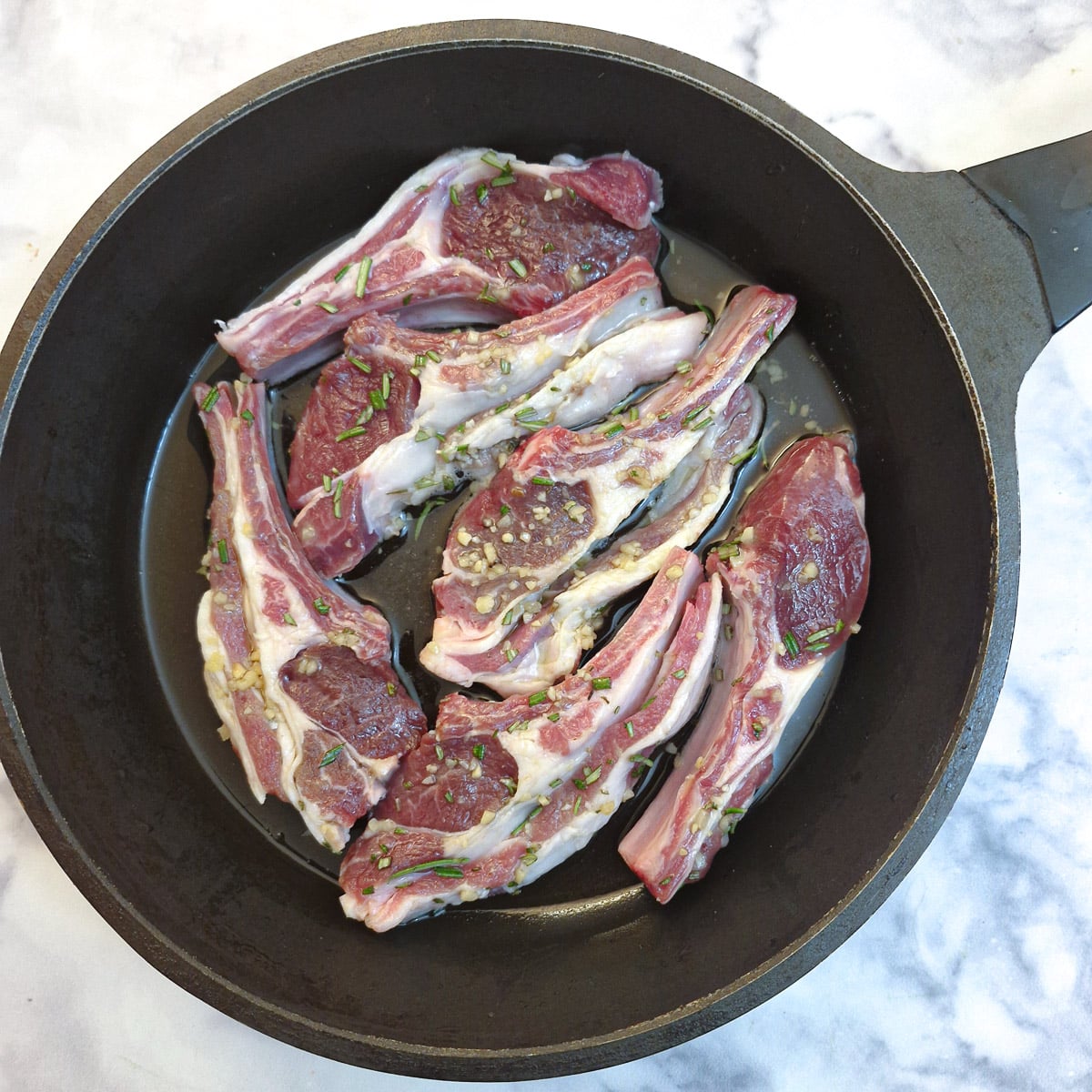 6 raw lamb chops in a frying pan.
