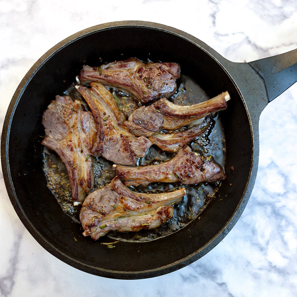 Six browned lamb chops in a frying pan.