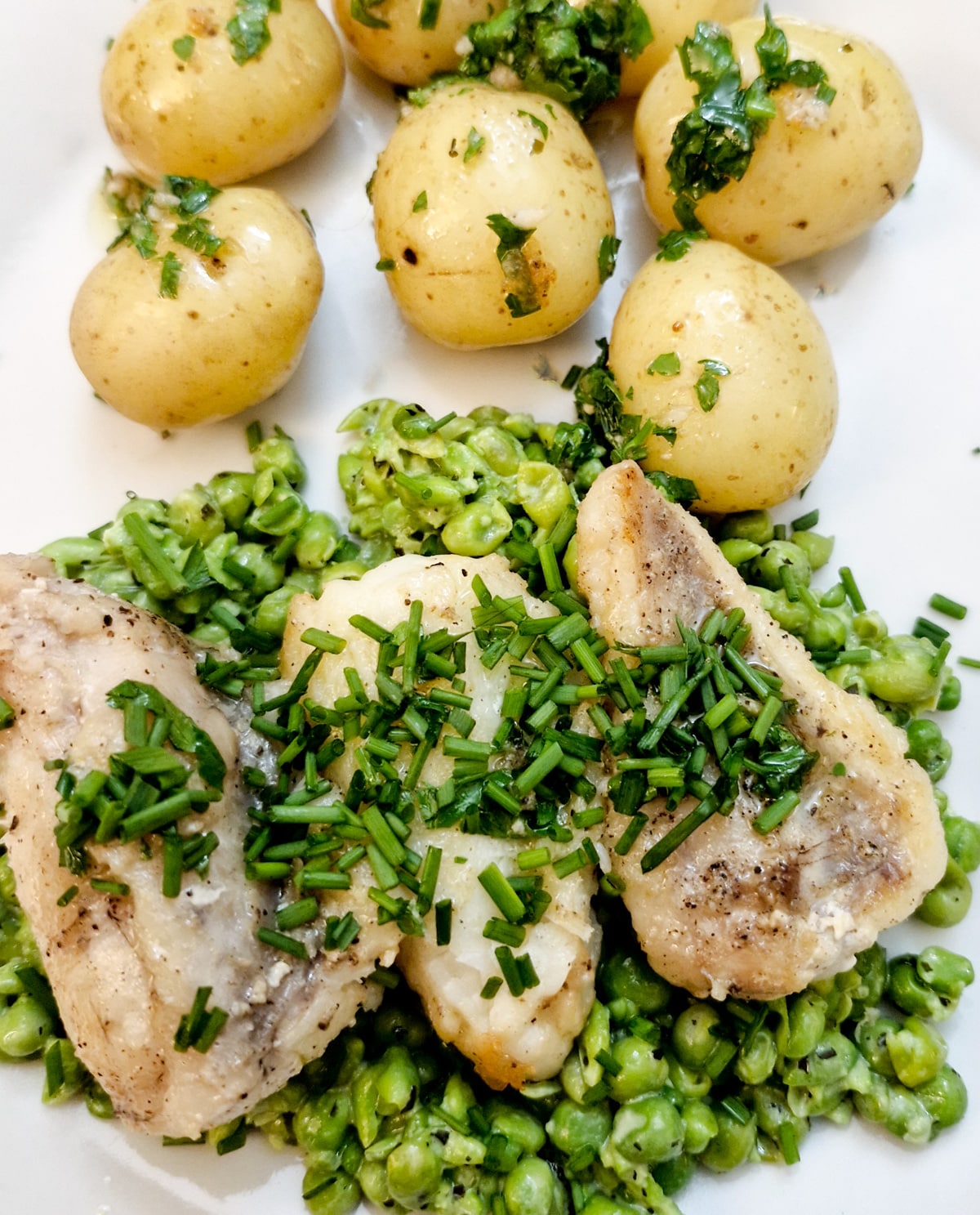 Three pieces of cooked monkfish on a bed of smashed minted peas with a helping of baby potatoes.