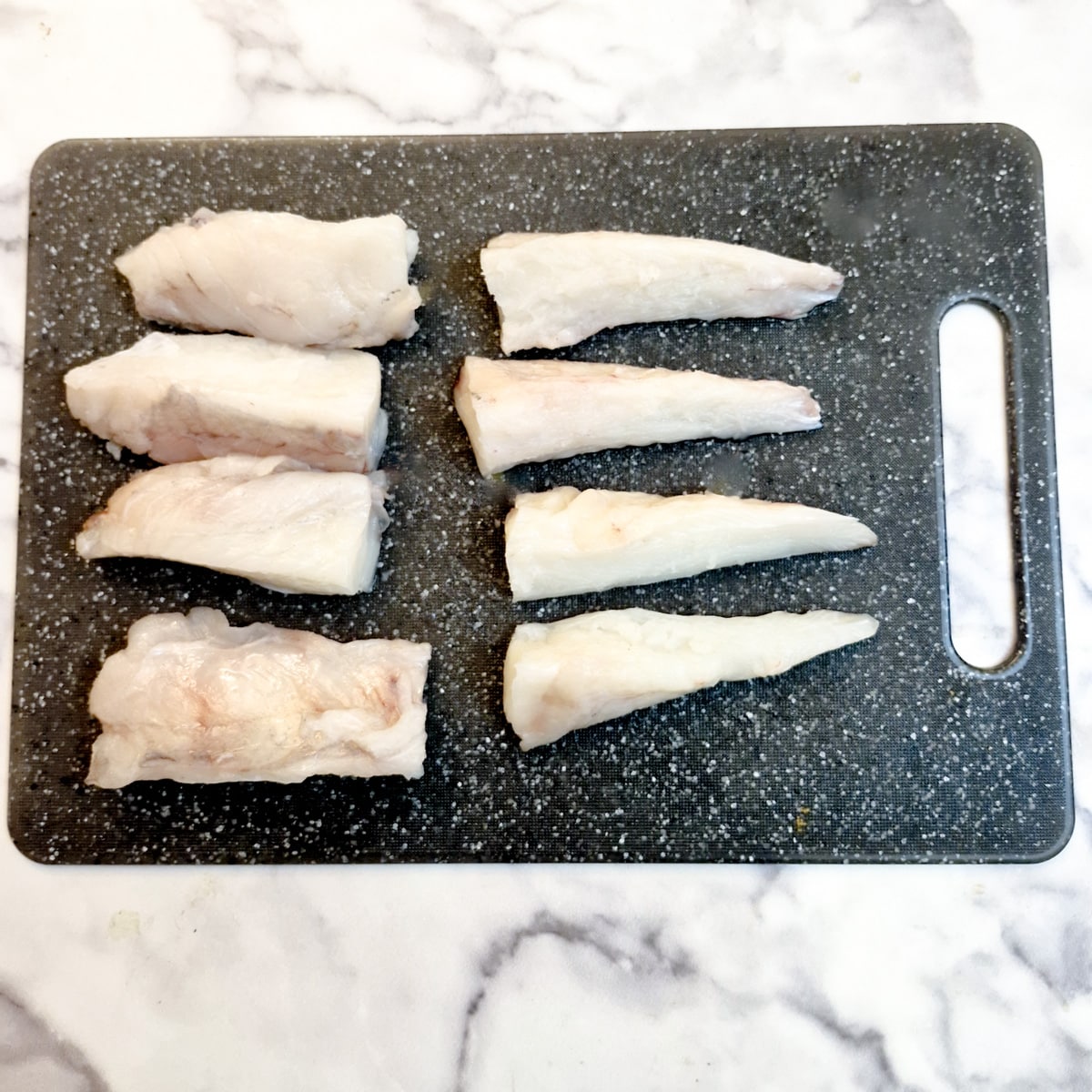 4 fillets of monkfish which have been cut in half, on a black chopping board.