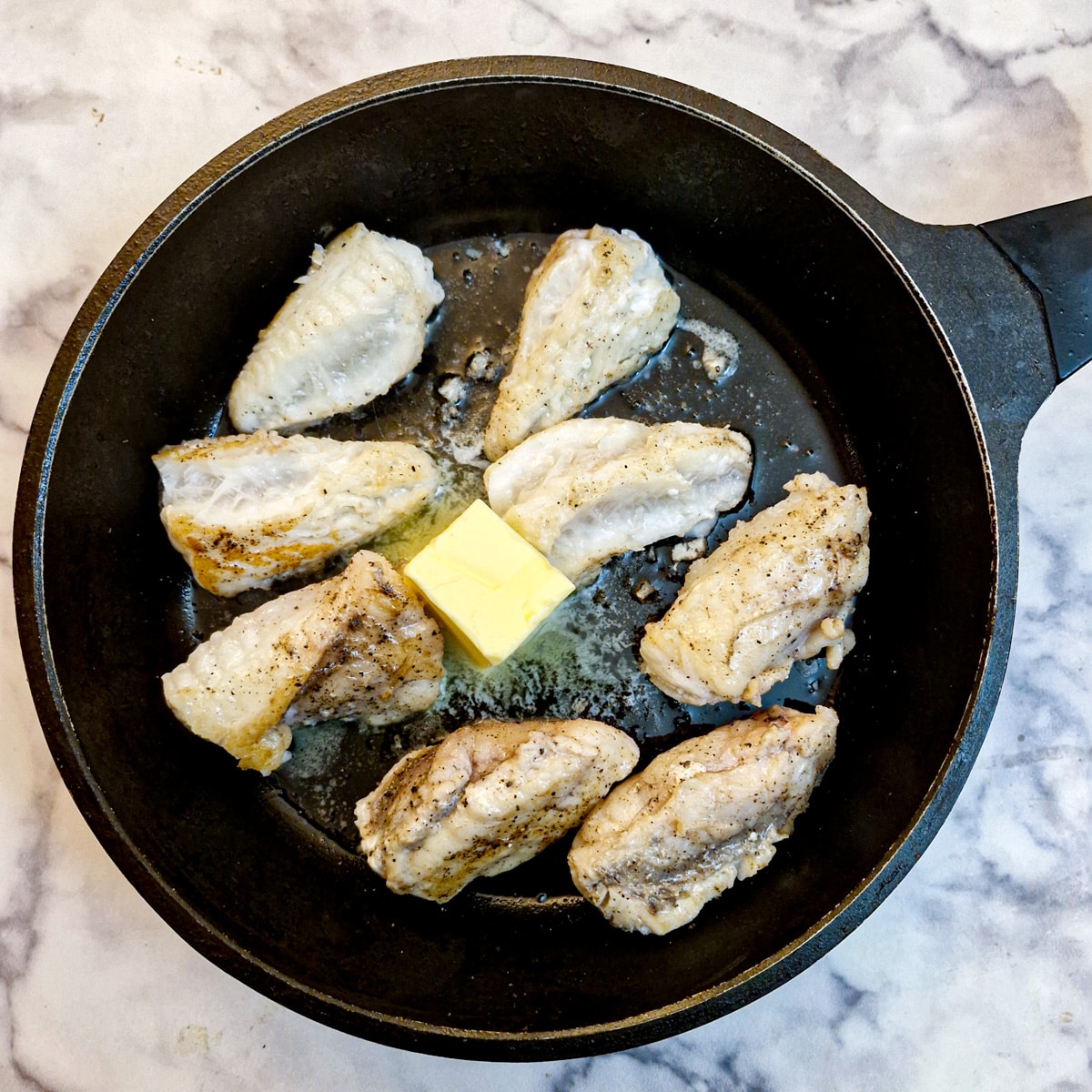 A knob of butter melting in a pan containing monkfish fillets.