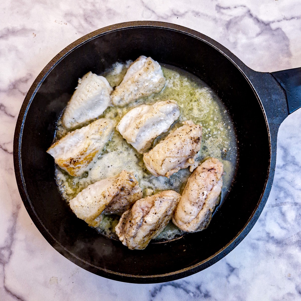 Fully cooked monkfish fillets in a frying pan.