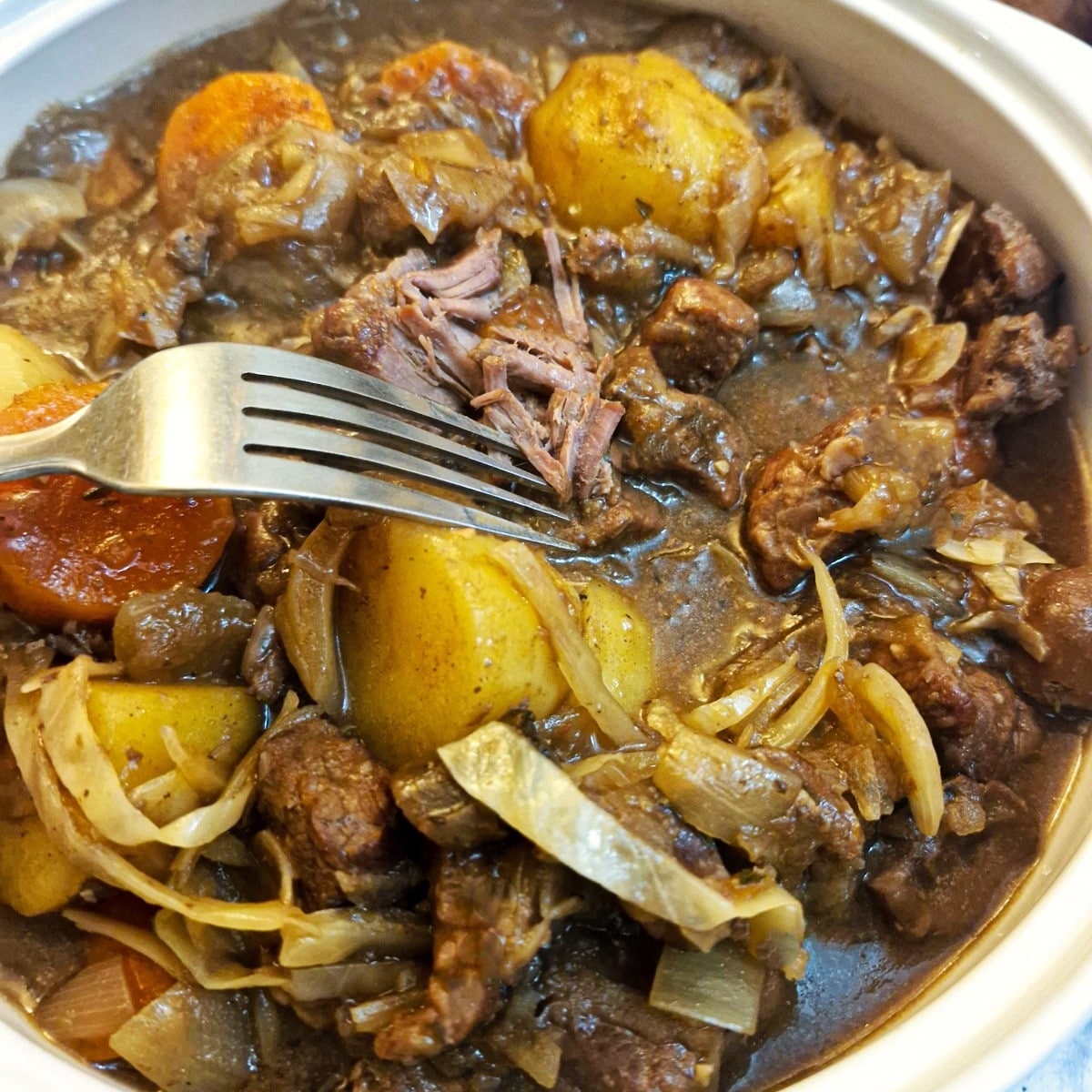 Closeup of a dish of beef and kidney stew showing the beef being shredded with a fork.