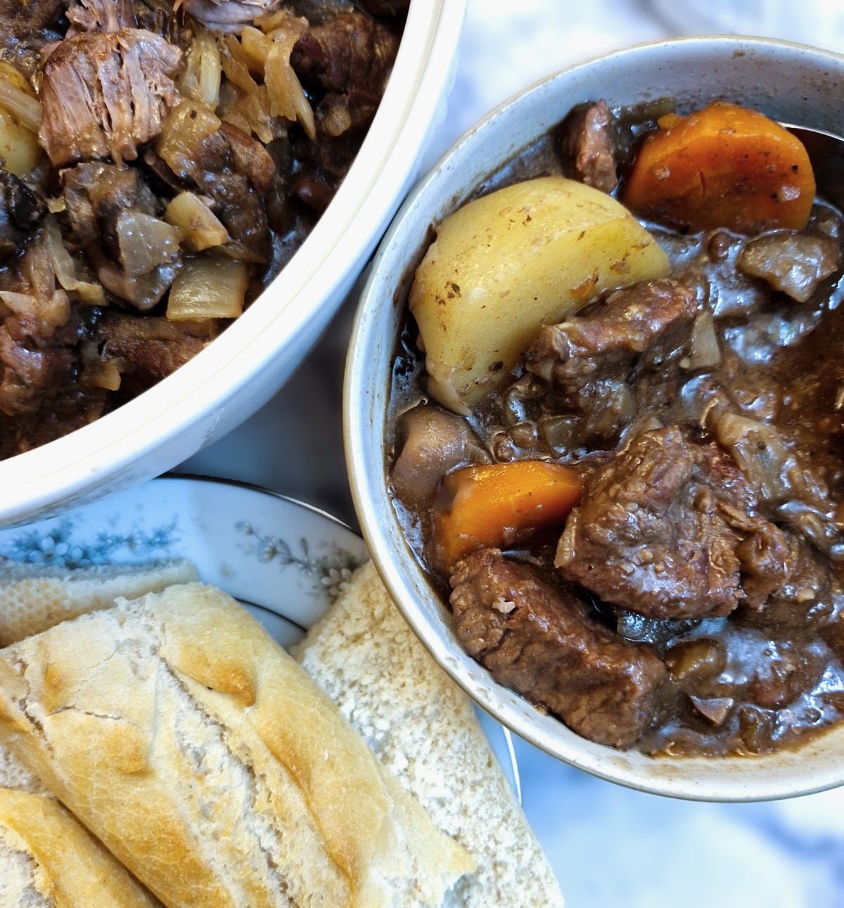 A bowl of beef and kidney stew next to a plate of crusty bread.