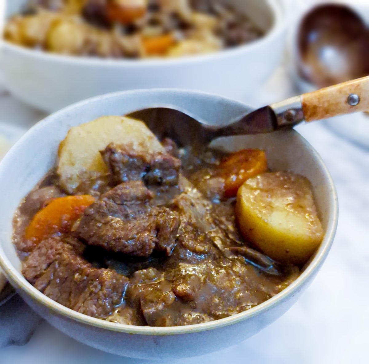 A small white dish with a helping of beef and kidney casserole and a spoon.